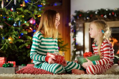 Mutlu küçük bir şömine karanlık bir odada rahat oturma tarafından Noel arifesinde oynarken Noel pijama giymiş kız kardeş. Xmas evde kutlama.
