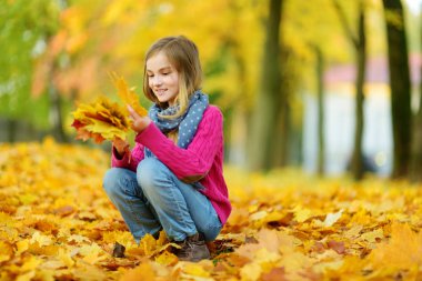 Sevimli küçük kız güzel sonbahar gününde eğleniyor. Sonbahar parkta oynayan mutlu çocuk. Sarı sonbahar yaprakları toplama çocuk. Çocuklar için sonbahar faaliyetleri.