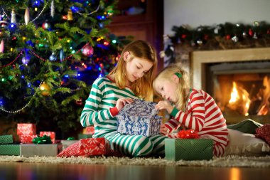 Mutlu küçük bir şömine karanlık bir odada rahat oturma tarafından Noel arifesinde oynarken Noel pijama giymiş kız kardeş. Xmas evde kutlama.