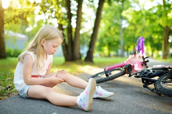 夏の公園で彼女の自転車から落ちて 後地面に座ってかわいい女の子 自転車に乗りながら怪我の子 子供と家族レジャー — ストック写真