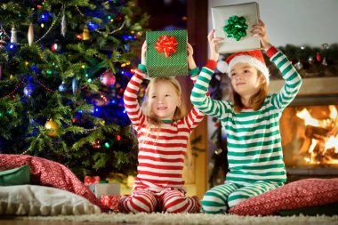 Mutlu küçük kız Noel arifesinde bir şömine karanlık bir odada rahat yaşam hediye kutuları açmalarına Noel pijama giyiyor. Xmas evde kutlama.