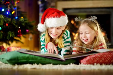 Mutlu küçük kız bir hikaye kitabı birlikte Noel arifesinde bir rahat karanlık oturma odasında şömine tarafından okuma. Xmas evde kutlama.