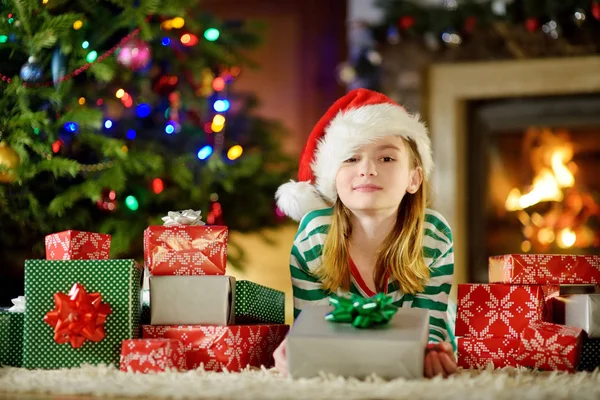 クリスマス イヴに 居心地の良い暗いリビング ルームの暖炉のそばで遊んでクリスマス パジャマを着て幸せな女の子 家庭でクリスマスを祝う — ストック写真