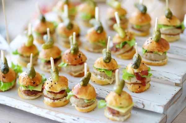 Delicious one bite mini burgers served on a party or wedding reception. Plates with assorted fancy finger food snacks on an event party or dinner.
