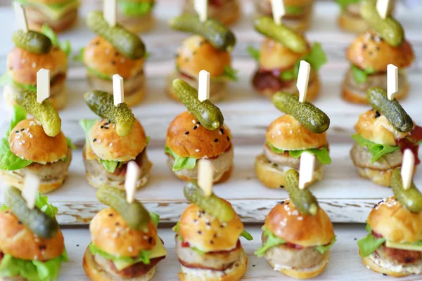 Delicious one bite mini burgers served on a party or wedding reception. Plates with assorted fancy finger food snacks on an event party or dinner.