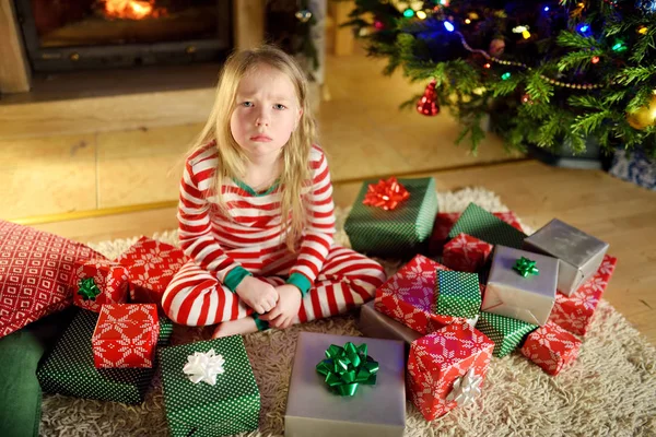 かわいい女の子は彼女のクリスマス プレゼントで不幸を感じてします クリスマス前夜 居心地の良い暗いリビング ルームの暖炉のそばで座っている子 あまりにも多くクリスマス プレゼント — ストック写真