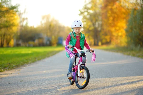 晴れた秋の日に公園で自転車に乗ってかわいい女の子 子供とアクティブなファミリー向けのレジャーです 自転車に乗りながら安全ヘメットを着て子供 — ストック写真