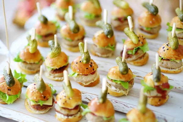 Delicious one bite mini burgers served on a party or wedding reception. Plates with assorted fancy finger food snacks on an event party or dinner.