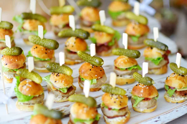 Delicious one bite mini burgers served on a party or wedding reception. Plates with assorted fancy finger food snacks on an event party or dinner.