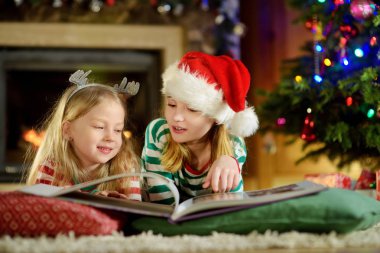 Mutlu küçük kız bir hikaye kitabı birlikte Noel arifesinde bir rahat karanlık oturma odasında şömine tarafından okuma. Xmas evde kutlama.
