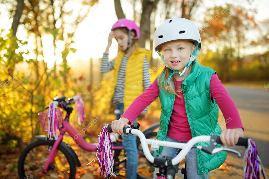 Cute little sisters riding bikes in a city park on sunny autumn day. Active family leisure with kids. Children wearing safety hemet while riding a bicycle.