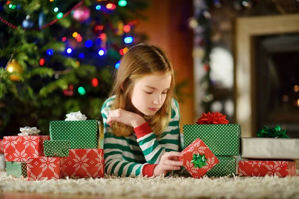 クリスマス イヴに 居心地の良い暗いリビング ルームの暖炉のそばで遊んでクリスマス パジャマを着て幸せな女の子 家庭でクリスマスを祝う — ストック写真