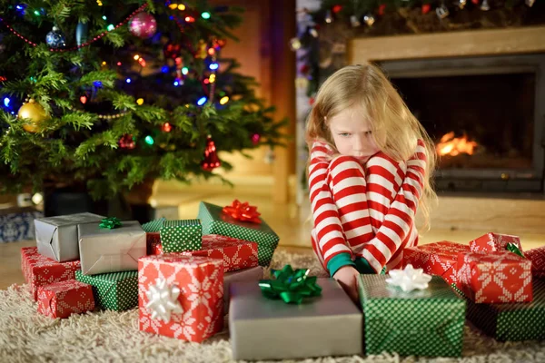 かわいい女の子は彼女のクリスマス プレゼントで不幸を感じてします クリスマス前夜 居心地の良い暗いリビング ルームの暖炉のそばで座っている子 あまりにも多くクリスマス プレゼント — ストック写真