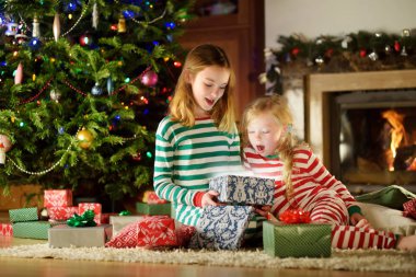 Mutlu küçük kız Noel arifesinde bir şömine karanlık bir odada rahat yaşam hediye kutuları açmalarına Noel pijama giyiyor. Xmas evde kutlama.