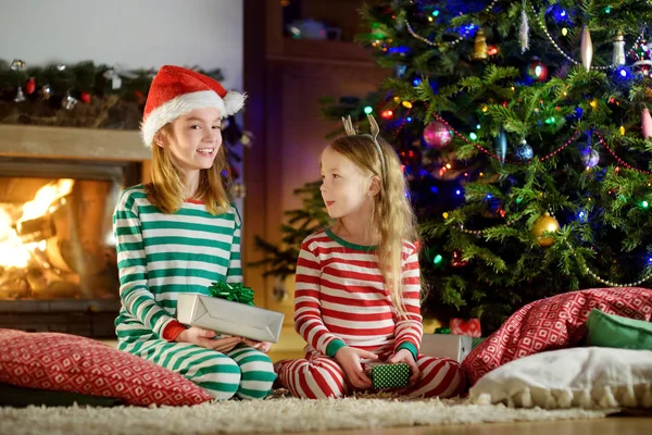 Hermanitas Felices Usando Pijamas Navidad Abriendo Cajas Regalo Junto Chimenea —  Fotos de Stock