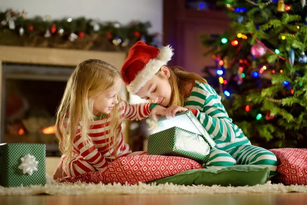 Mutlu küçük rahat karanlık oturma odasında şömine tarafından hediye kutuları açma Noel pijama giymiş kız kardeş 