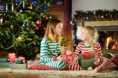 Mutlu küçük rahat karanlık oturma odasında şömine tarafından hediye kutuları açma Noel pijama giymiş kız kardeş 