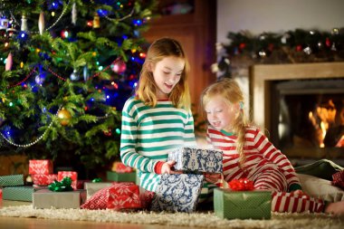 Mutlu küçük rahat karanlık oturma odasında şömine tarafından hediye kutuları açma Noel pijama giymiş kız kardeş 