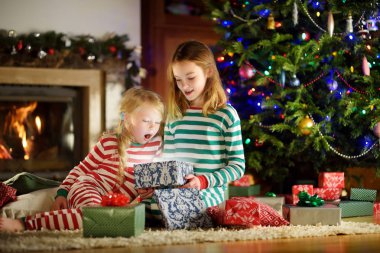 Mutlu küçük rahat karanlık oturma odasında şömine tarafından hediye kutuları açma Noel pijama giymiş kız kardeş 