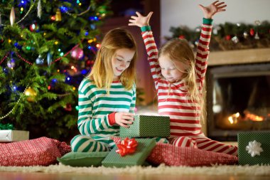 Mutlu küçük rahat karanlık oturma odasında şömine tarafından hediye kutuları açma Noel pijama giymiş kız kardeş 