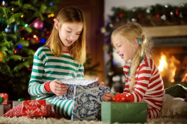 Mutlu küçük rahat karanlık oturma odasında şömine tarafından hediye kutuları açma Noel pijama giymiş kız kardeş 