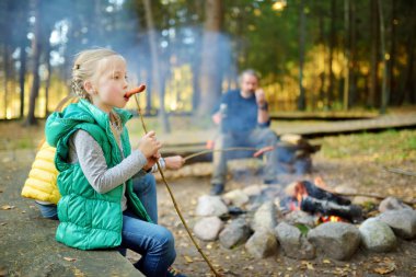 Sevimli küçük kız ve baba kavurma hot-dogs şenlik ateşi dal üzerinde