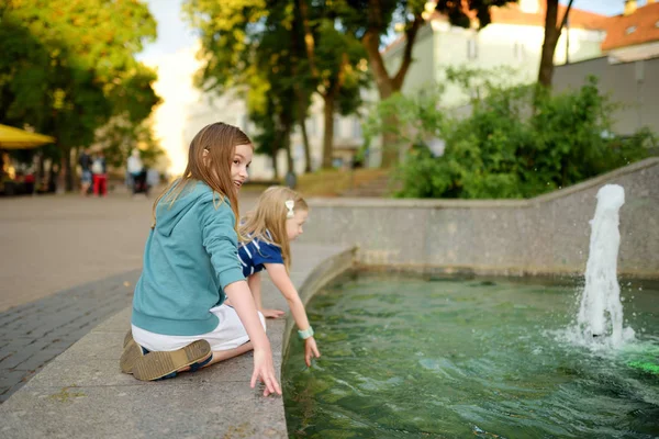 两个可爱的小女孩在城市喷泉玩在炎热和阳光明媚的夏日 — 图库照片