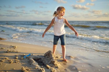 Sevimli küçük kız eğleniyor kumsalda sıcak ve güneşli yaz gününde deniz kenarında