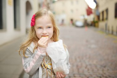 Sevimli küçük kız taze pişmiş çerezleri sıcak ve güneşli yaz gününde yeme Vilnius, Litvanya