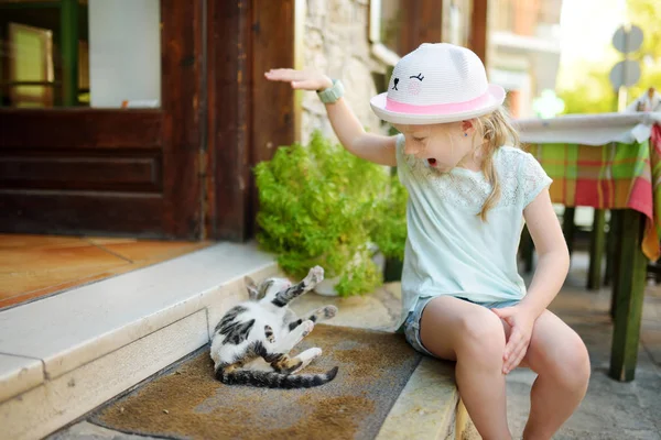 可爱的年轻女孩抚摸一个友好的希腊猫在温暖和阳光明媚的夏日家庭度假在卡拉夫里塔村 — 图库照片