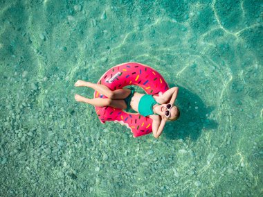 Aerial top down view of cute young girl floating on toy ring at Myrtos beach, the most beautiful beach of Kefalonia, a large coast with turqoise water and white coarse sand. Cephalonia, Greece. clipart