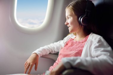 Sevimli genç kız bir uçakla seyahat. Uçak cam kenarında oturan ve müzik dinlerken dışında arayan çocuk. Yurt dışında çocuklar seyahat.