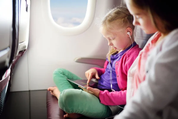 Adorable little girls traveling by an airplane. Children sitting by aircraft window and using a digital tablet during the flight. Traveling abroad with kids.