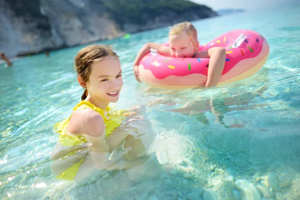 可爱的姐妹漂浮在玩具环在 Myrtos 凯法利尼亚最著名和最美丽的海滩 一个大海岸与绿茶水和白色粗糙的沙子 希腊头孢罗尼亚 — 图库照片