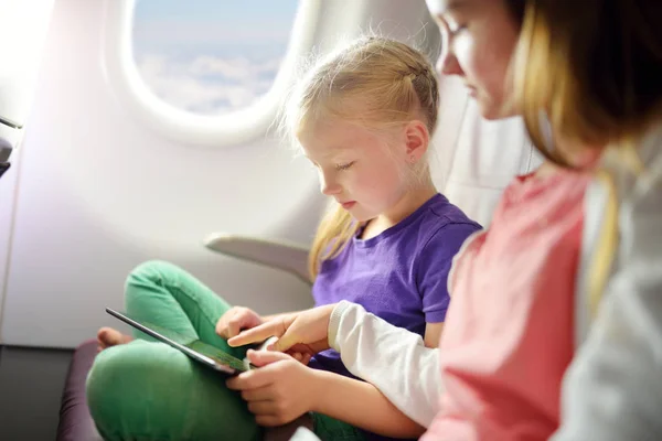 Adorable little girls traveling by an airplane. Children sitting by aircraft window and using a digital tablet during the flight. Traveling abroad with kids.