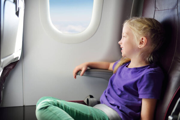 Adorable little girl traveling by an airplane. Child sitting by aircraft window and looking outside. Traveling abroad with kids.