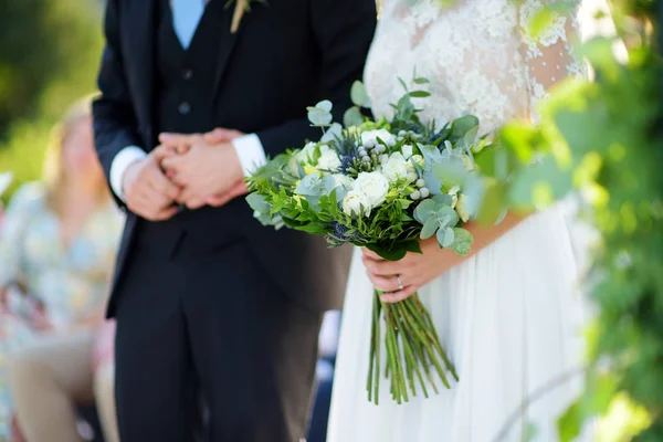 Sposa che tiene un bellissimo bouquet da sposa durante la cerimonia nuziale nella soleggiata giornata estiva all'aperto . — Foto Stock