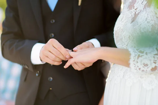 Groom putting wedding ring on bride's finger during wedding ceremony outdoors on beautiful summer day. — Stock Photo, Image