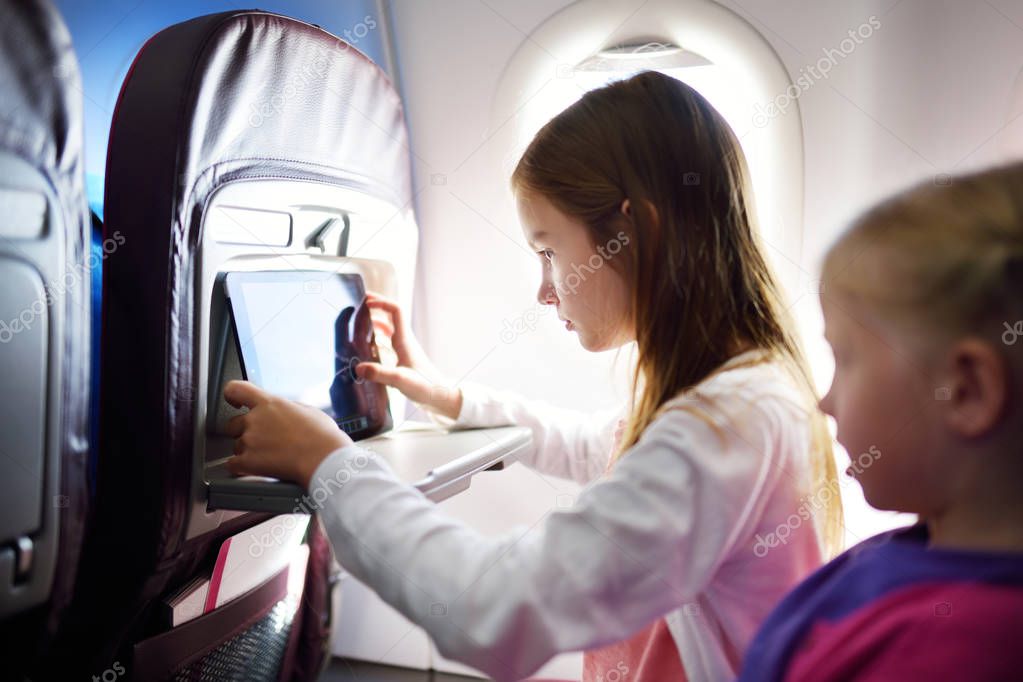 Adorable little girls traveling by an airplane. Children sitting by aircraft window and using a digital tablet during the flight. Traveling abroad with kids.