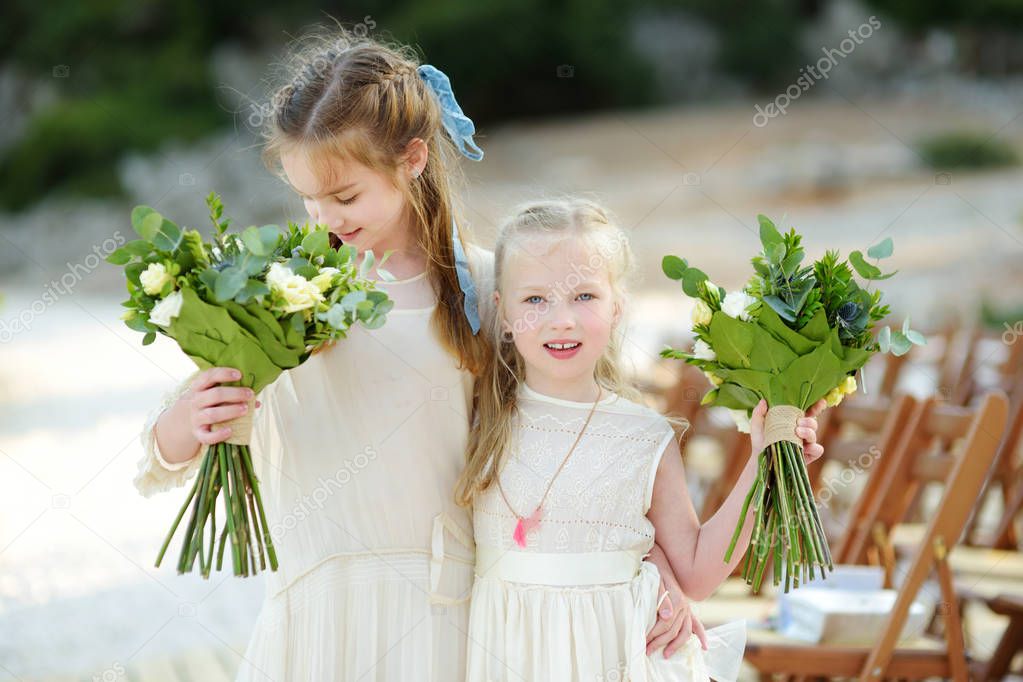 Two adorable young bridesmaids holding beautiful flower bouquets after wedding cemerony outdoors. Destination wedding on Cephalonia island on Greece.