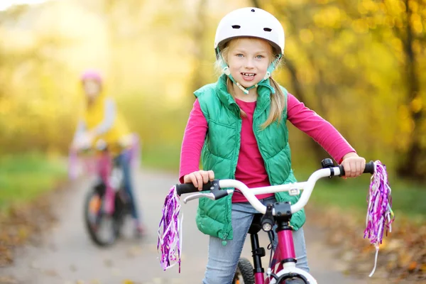 Niedlichen kleinen Schwestern auf Fahrrädern in einem Stadtpark an einem sonnigen Herbsttag. Aktive Familienfreizeit mit Kindern. — Stockfoto