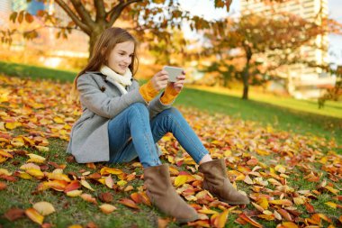 Güzel sonbahar gününde eğlenen sevimli genç kız. Sonbahar parkında oynayan mutlu çocuk. Sarı sonbahar yaprakları toplayan çocuk.
