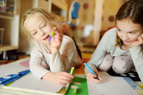 Två söta små systrar skriver brev tillsammans hemma. Äldre syster hjälpa unge med hennes läxor. — Stockfoto
