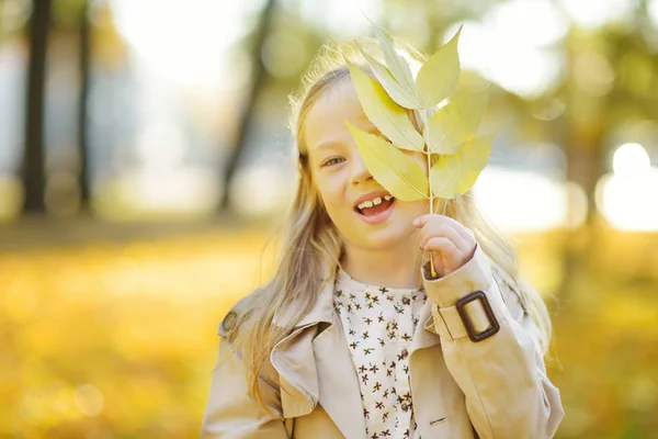 Entzückende junge Mädchen, die Spaß an einem schönen Herbsttag haben. glückliches Kind, das im Herbstpark spielt. Kind sammelt gelbes Herbstlaub. — Stockfoto