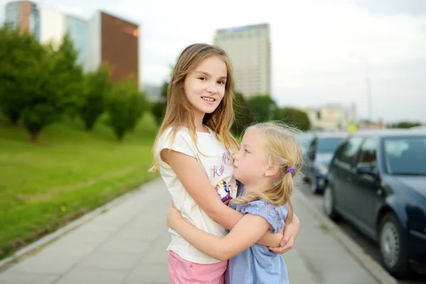 Zwei entzückende Schwestern lachen und umarmen sich an einem warmen und sonnigen Sommertag in einer Stadt. — Stockfoto