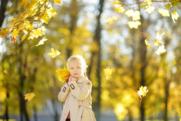 Imádnivaló fiatal lány birtoklás móka-ra szép őszi napon. Boldog gyermek játszik az őszi parkban. Gyerek összegyűjtése sárga Lombhullás. — Stock Fotó
