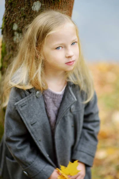 Adorabile ragazza che si diverte nella bella giornata autunnale. Bambino felice che gioca nel parco autunnale. Ragazzo raccolta fogliame caduta gialla . — Foto Stock