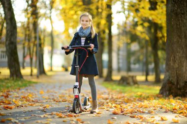 Sevimli genç kız güneşli sonbahar akşamı bir şehir parkında onu scooter sürme. Pretty preteen çocuk bir rulo sürme.