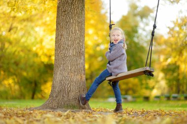 Sevimli genç kız güneşli sonbahar parkta bir salıncak ta eğleniyor. Bir şehirde aile hafta sonu.
