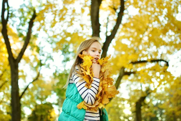 Menina adorável se divertindo no belo dia de outono. Criança feliz brincando no parque de outono. Criança recolhendo folhagem queda amarela . — Fotografia de Stock